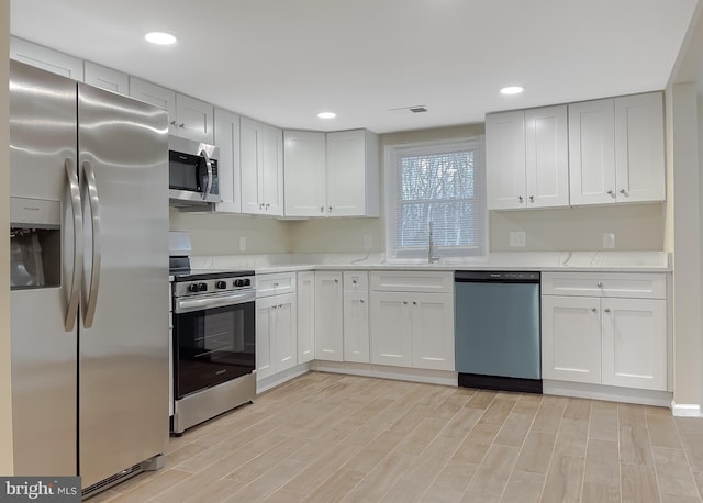 kitchen with light wood-type flooring, light stone counters, stainless steel appliances, sink, and white cabinetry