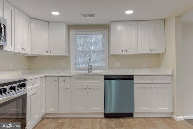 kitchen featuring white cabinets, appliances with stainless steel finishes, light stone counters, and sink