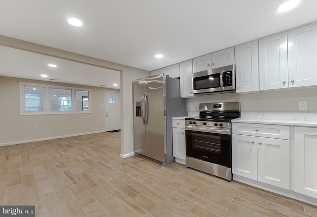 kitchen featuring light stone counters, white cabinets, stainless steel appliances, and light wood-type flooring