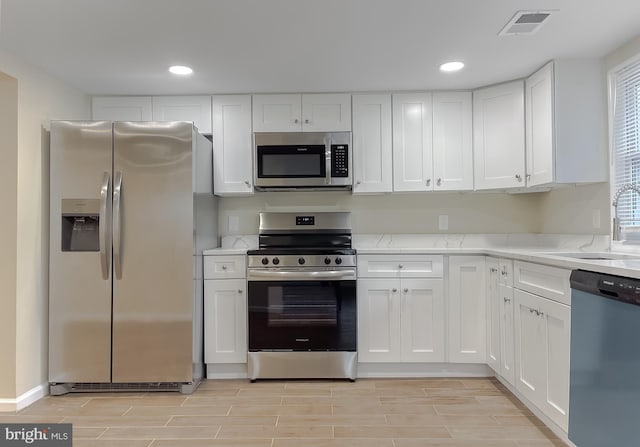 kitchen featuring white cabinets, appliances with stainless steel finishes, light stone countertops, and sink