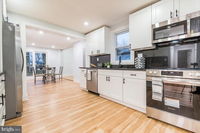 kitchen with white cabinets, decorative backsplash, light hardwood / wood-style floors, and appliances with stainless steel finishes