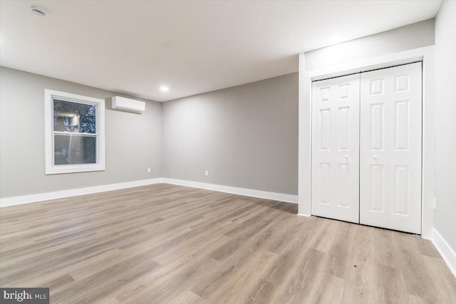 unfurnished bedroom featuring a wall mounted air conditioner, light hardwood / wood-style floors, and a closet