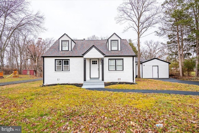 cape cod-style house with a front yard and an outbuilding