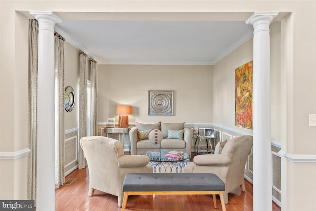 living area with decorative columns, crown molding, and hardwood / wood-style floors