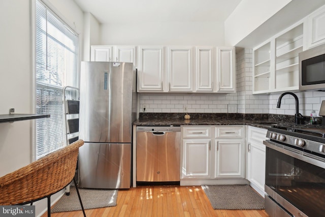 kitchen featuring stainless steel appliances, glass insert cabinets, light wood-type flooring, and white cabinetry