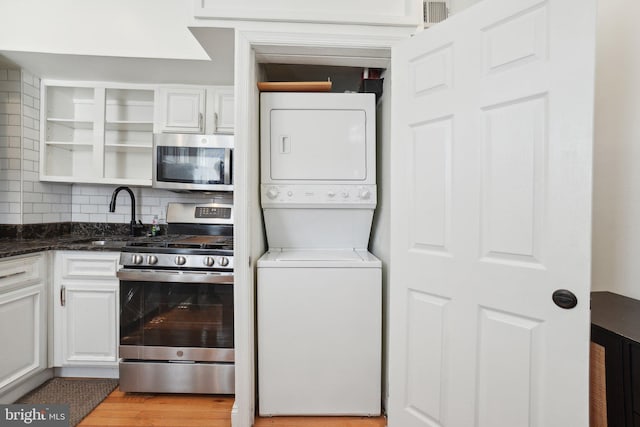 kitchen featuring a sink, white cabinets, appliances with stainless steel finishes, stacked washer and clothes dryer, and glass insert cabinets