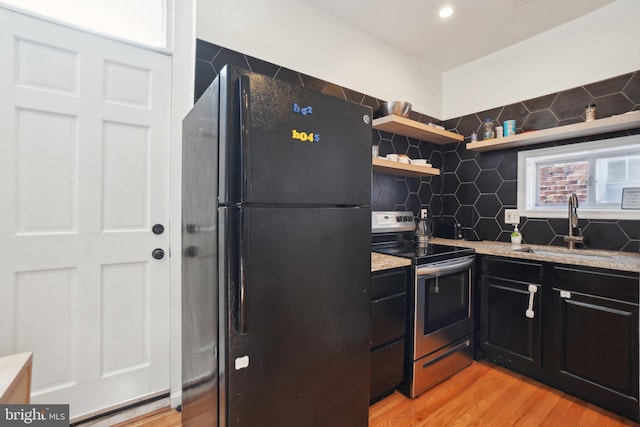 kitchen with a sink, stainless steel range with electric cooktop, dark cabinetry, freestanding refrigerator, and open shelves