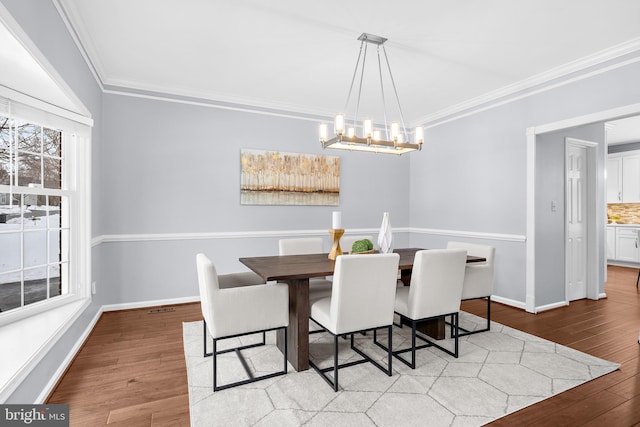 dining space with light wood-type flooring, a notable chandelier, and crown molding