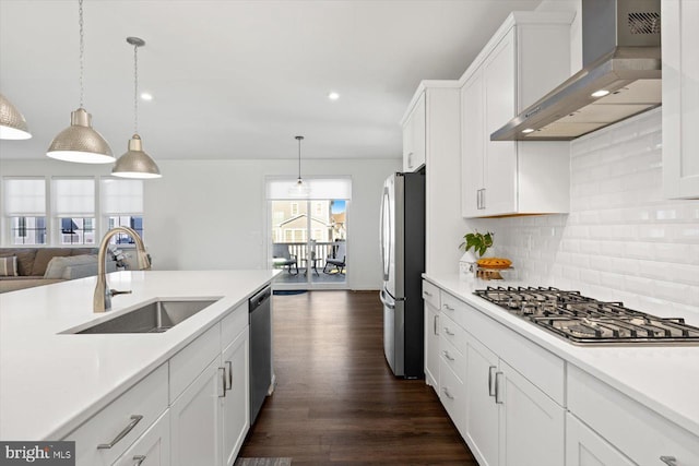 kitchen featuring pendant lighting, sink, wall chimney exhaust hood, white cabinetry, and stainless steel appliances