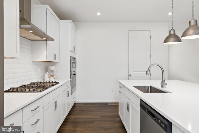 kitchen with white cabinetry, sink, stainless steel appliances, wall chimney range hood, and decorative light fixtures