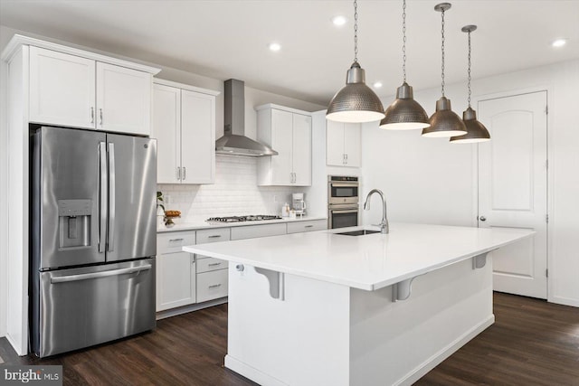 kitchen with pendant lighting, stainless steel appliances, a center island with sink, and wall chimney range hood