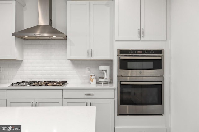 kitchen with white cabinets, decorative backsplash, wall chimney range hood, and stainless steel appliances