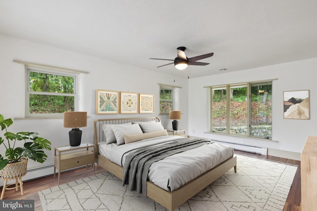 bedroom with ceiling fan, light hardwood / wood-style floors, a baseboard radiator, and multiple windows