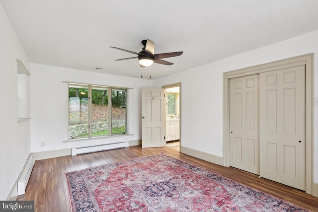 unfurnished bedroom featuring wood-type flooring, a closet, baseboard heating, and ceiling fan