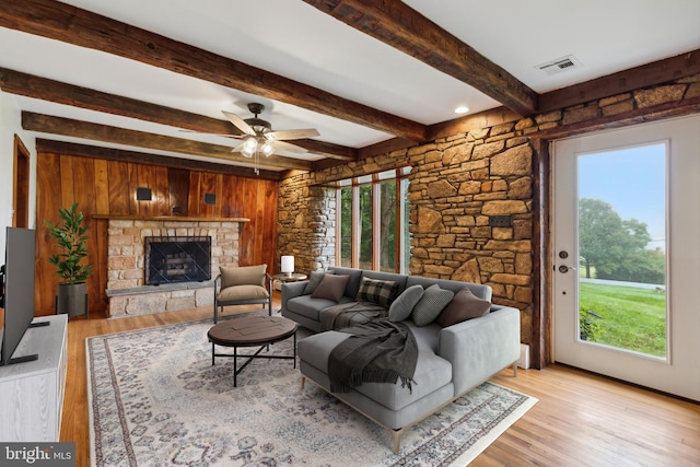 living room with beamed ceiling, light hardwood / wood-style floors, a fireplace, and wooden walls