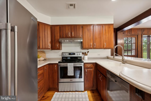 kitchen with beam ceiling, sink, stainless steel appliances, and light hardwood / wood-style flooring