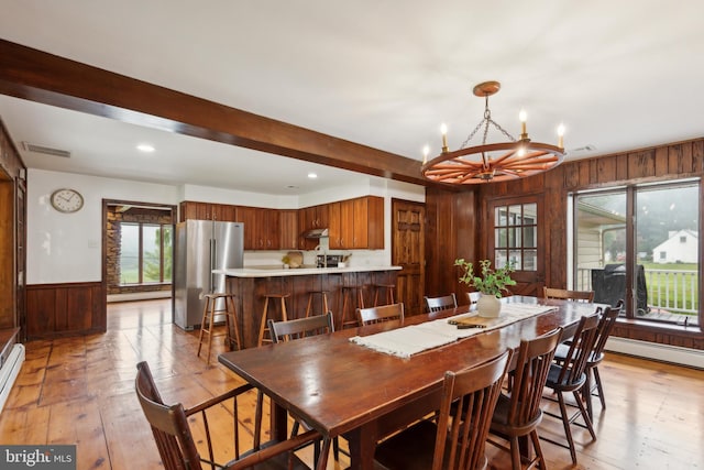 dining area with wood walls, a baseboard heating unit, beam ceiling, a notable chandelier, and light hardwood / wood-style floors