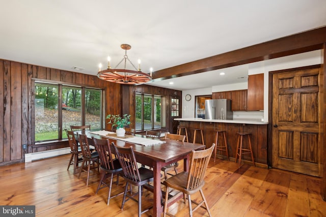 dining area featuring a baseboard radiator, beamed ceiling, a notable chandelier, wooden walls, and light wood-type flooring