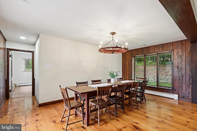 dining space with a chandelier, light hardwood / wood-style floors, baseboard heating, and wooden walls