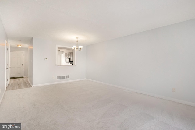 spare room with light colored carpet and a notable chandelier