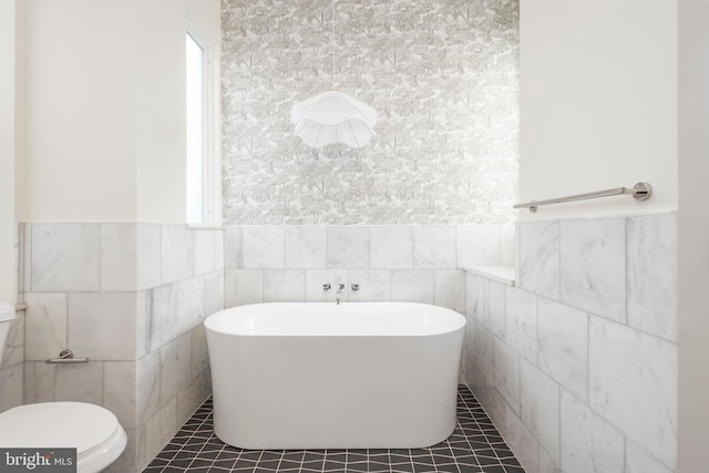 bathroom with a bathing tub, toilet, tile walls, and tile patterned floors