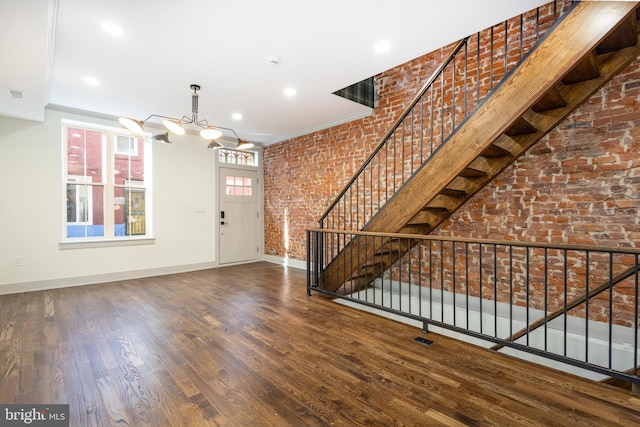 foyer entrance featuring dark hardwood / wood-style flooring, a notable chandelier, crown molding, and brick wall