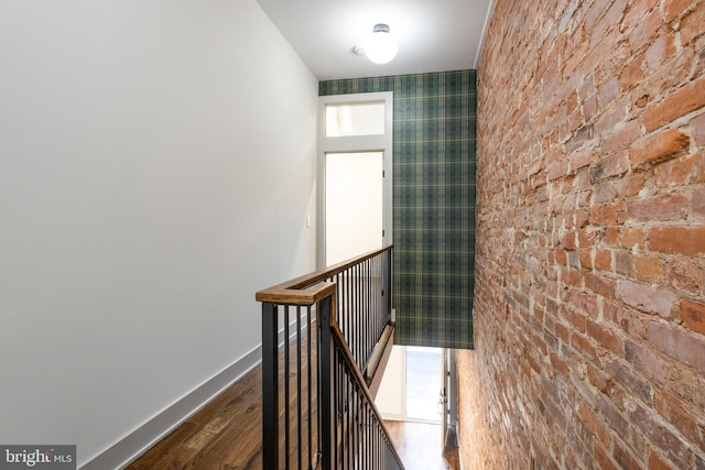 stairway with hardwood / wood-style flooring, a healthy amount of sunlight, and brick wall