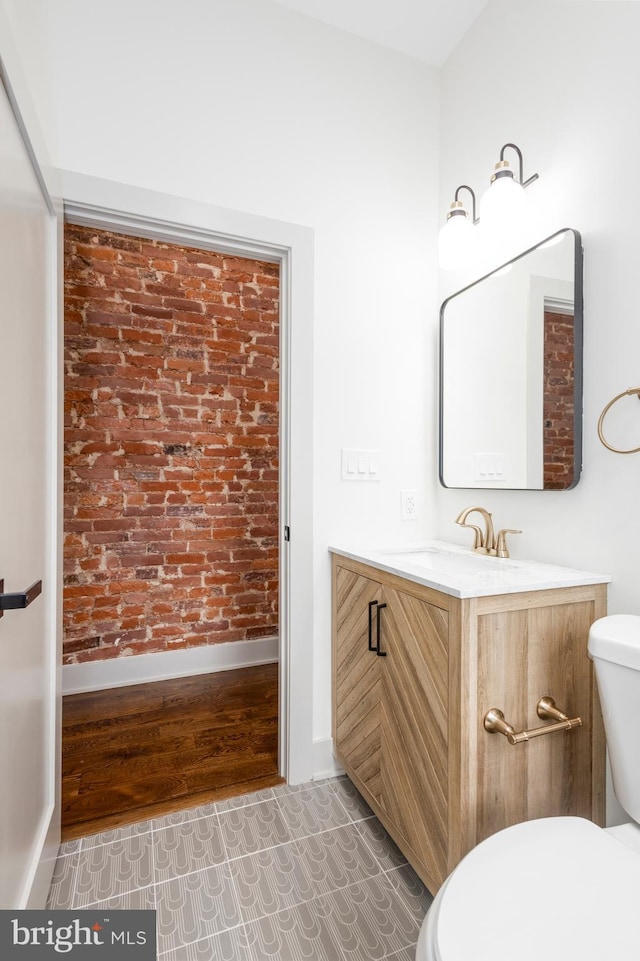 bathroom with tile patterned floors, vanity, brick wall, and toilet