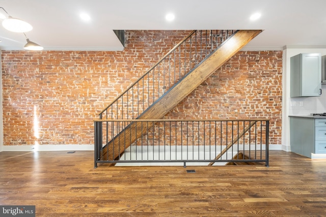 unfurnished living room with hardwood / wood-style floors, ornamental molding, and brick wall