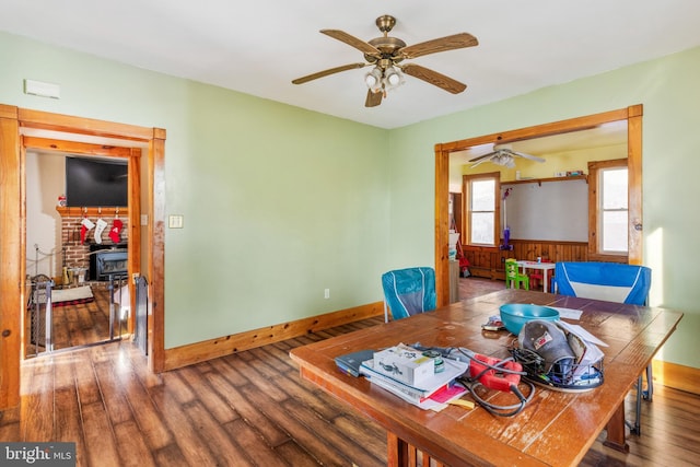 dining space with wood-type flooring, a wood stove, ceiling fan, and wood walls