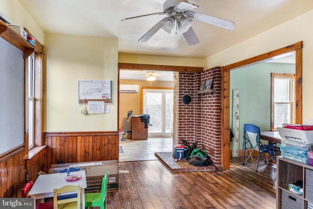 interior space with ceiling fan, hardwood / wood-style flooring, an AC wall unit, a wood stove, and wood walls