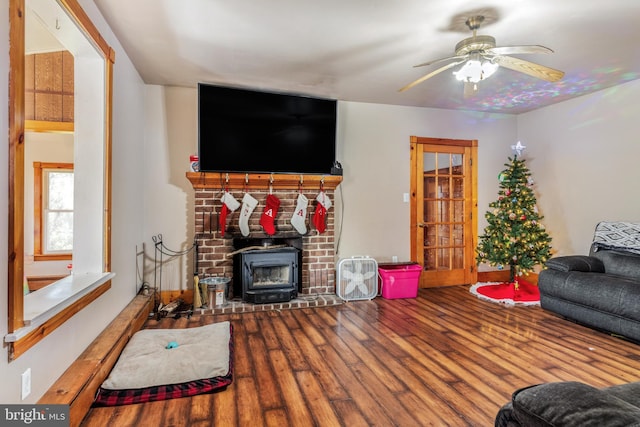 living room featuring wood-type flooring, a wood stove, and ceiling fan