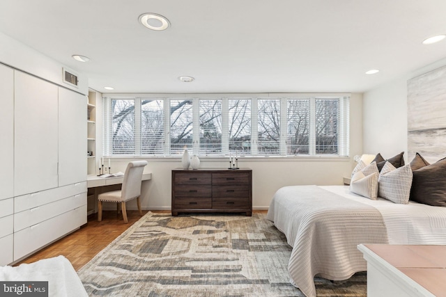 bedroom with a closet, built in desk, multiple windows, and light parquet floors