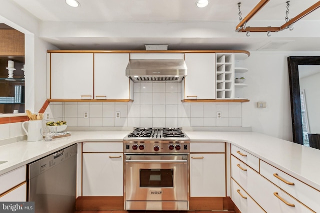 kitchen featuring kitchen peninsula, tasteful backsplash, wall chimney exhaust hood, stainless steel appliances, and white cabinetry