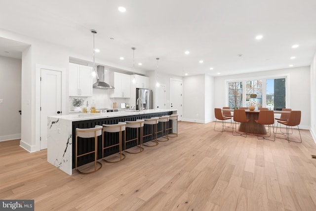 kitchen featuring white cabinetry, hanging light fixtures, stainless steel fridge with ice dispenser, a large island, and wall chimney exhaust hood