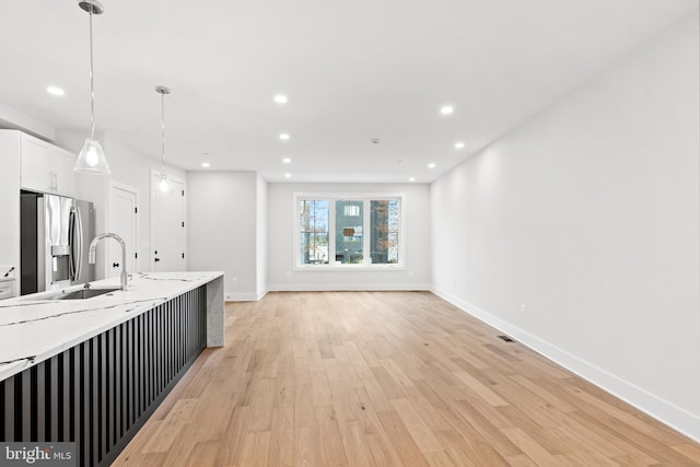 kitchen with white cabinetry, hanging light fixtures, stainless steel fridge, light stone counters, and light hardwood / wood-style flooring