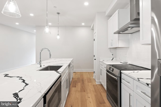 kitchen featuring white cabinetry, stainless steel appliances, hanging light fixtures, wall chimney exhaust hood, and light stone counters