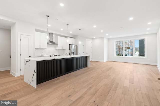 kitchen with white cabinetry, stainless steel fridge, a large island, hanging light fixtures, and wall chimney range hood