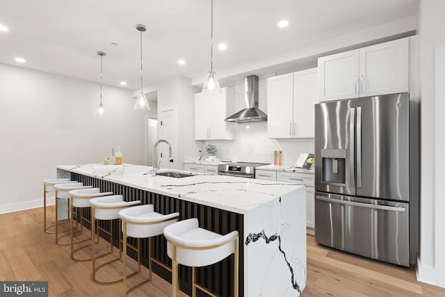 kitchen with appliances with stainless steel finishes, a kitchen island with sink, wall chimney range hood, white cabinets, and sink