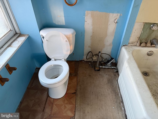 bathroom with a washtub, toilet, and parquet floors