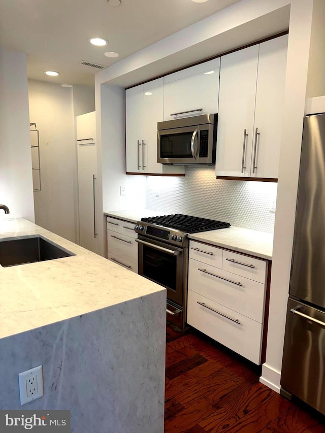 kitchen featuring white cabinetry, sink, dark wood-type flooring, decorative backsplash, and appliances with stainless steel finishes