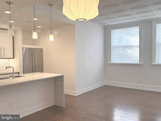 kitchen featuring sink, light stone countertops, high quality fridge, decorative light fixtures, and dark hardwood / wood-style flooring