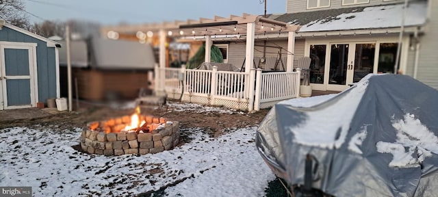 view of snowy exterior featuring a wooden deck, french doors, a fire pit, and a storage unit