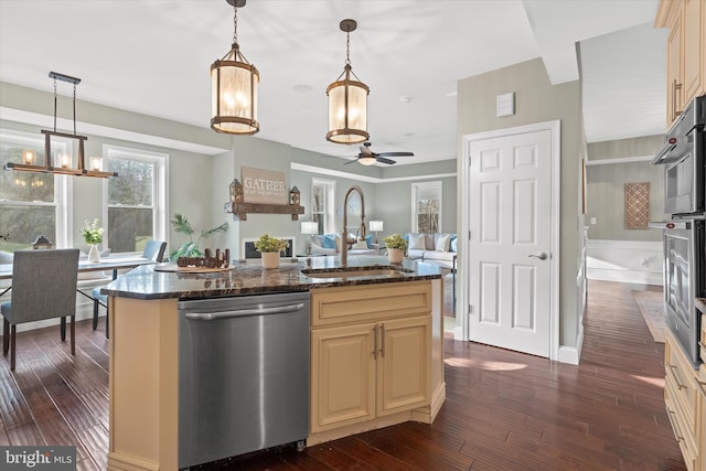 kitchen featuring appliances with stainless steel finishes, dark stone counters, ceiling fan, sink, and a center island with sink