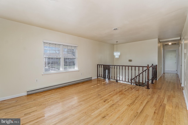 empty room featuring light wood-type flooring, baseboard heating, and a chandelier