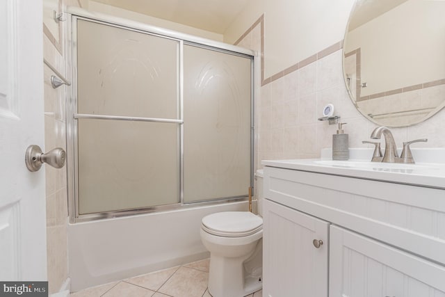 full bathroom with vanity, combined bath / shower with glass door, tile patterned flooring, toilet, and tile walls