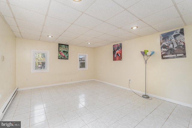 basement featuring light tile patterned floors, a drop ceiling, and baseboard heating