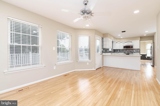 kitchen with white cabinets, kitchen peninsula, appliances with stainless steel finishes, and light hardwood / wood-style flooring