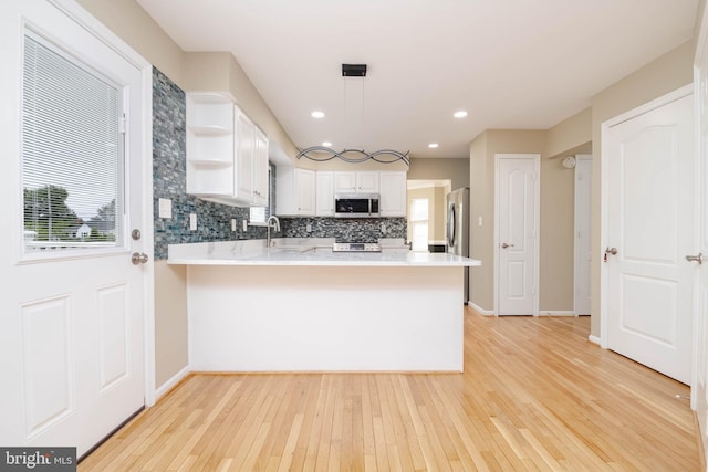 kitchen featuring kitchen peninsula, light hardwood / wood-style floors, pendant lighting, white cabinets, and appliances with stainless steel finishes