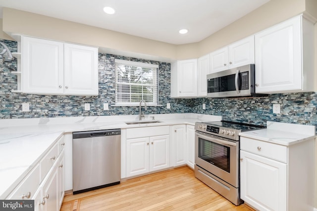 kitchen with sink, backsplash, light hardwood / wood-style floors, white cabinets, and appliances with stainless steel finishes